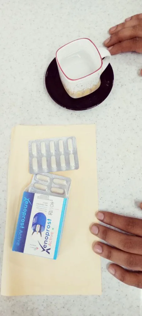 Blíster de 10 cápsulas blancas junto a la caja de Xenoprost Active y una taza