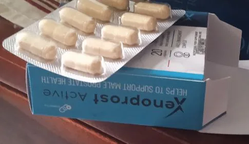 Caja de Xenoprost Active abierta y blíster con cápsulas sobre un mueble de madera